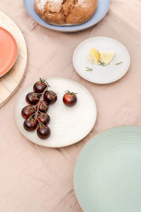 Plates in different colours on a table decorates with tomatos and a bread
