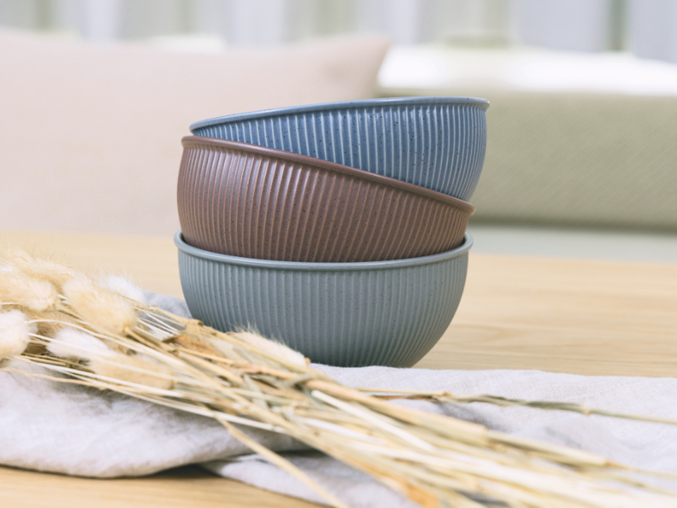 Japandi-style tableware by Thomas, featuring ribbed bowls in shades of blue, grey and brown, on a light wooden table.