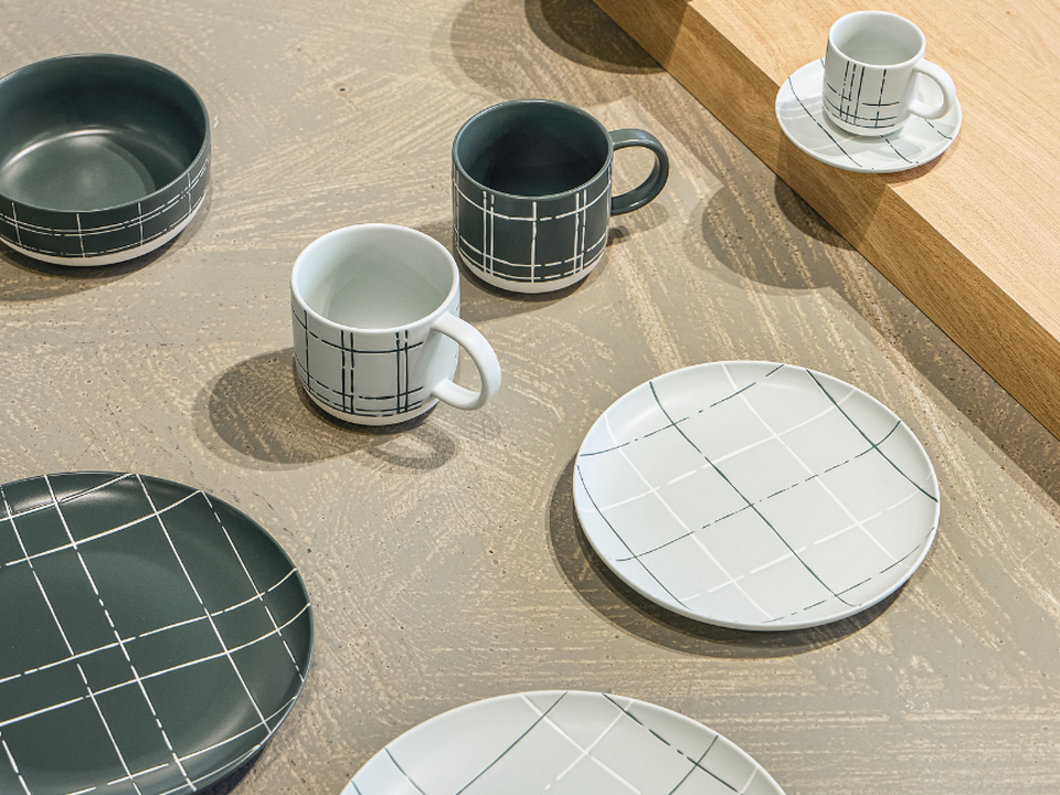 Japandi-style tableware by Thomas, featuring checked cups, plates and bowls in white and dark shades, arranged on a wooden table.
