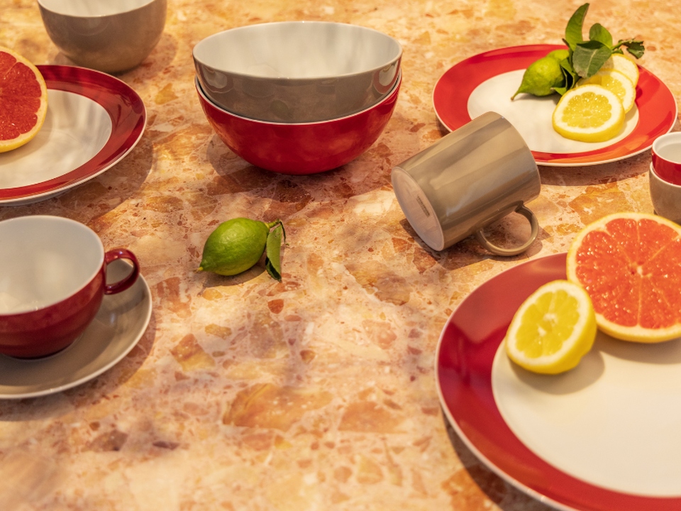 A brunch scene featuring Thomas tableware in rich shades of red and cream: plates, cups and bowls are arranged on a warm stone surface, accompanied by fresh citrus fruits such as grapefruit, lemon and lime. The combination of vibrant tableware and fresh ingredients creates a lively, modern table setting.