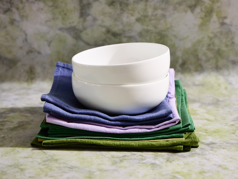 Two white bowls by Thomas Sensai, stacked on top of a pile of colourful linen cloths