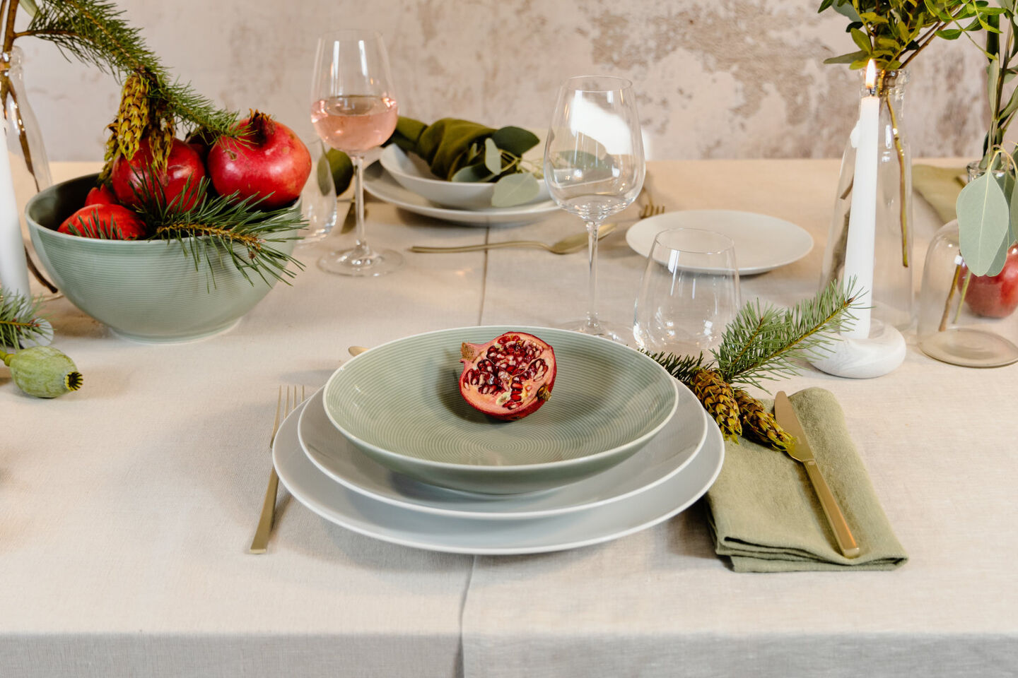 Halber Granatapfel auf dezent grünem Suppenteller, auf zwei weißen Speisetellern auf einem weihnachtlich gedeckten Tisch