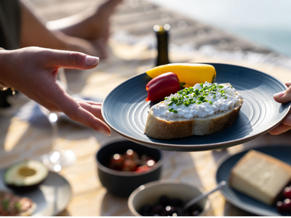 A close-up of a brunch scene featuring Thomas tableware: a hand is holding out a dark blue, modern-style plate with a sandwich garnished with radishes.