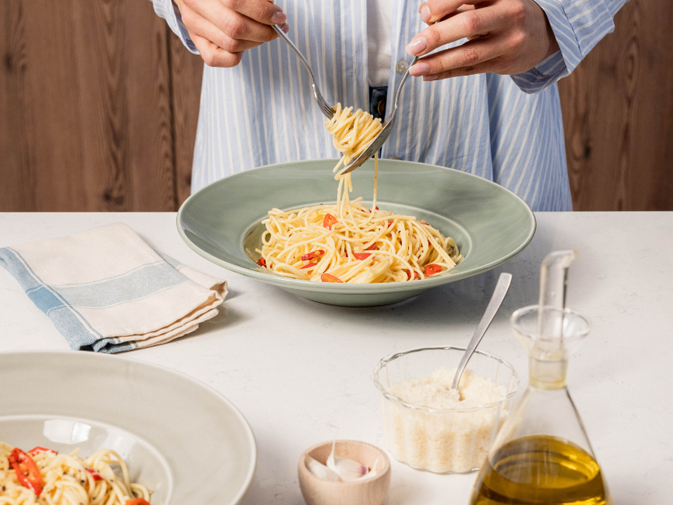 Spaghetti aglio e olio dans une assiette verte Thomas, servis avec parmesan et huile d’olive