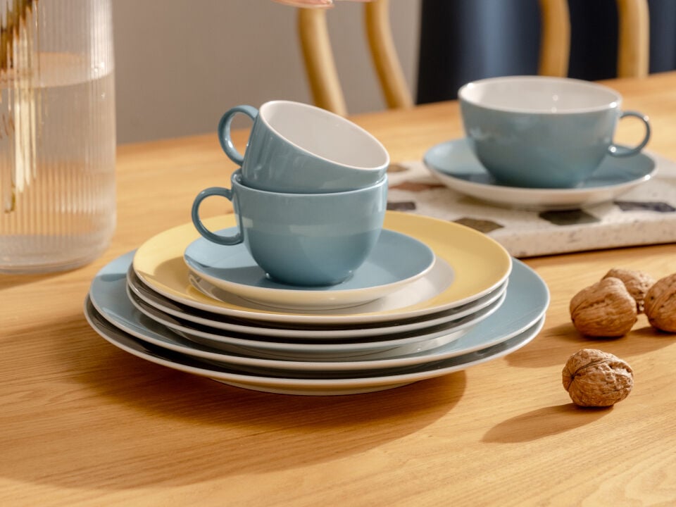 Thomas Sunny Day Teller und Tassen aufeinandergestapelt auf einem Holztisch neben Waln&uuml;ssen