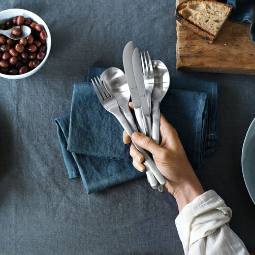 Hand holding shiny WMF cutlery above a laid table with a linen tablecloth