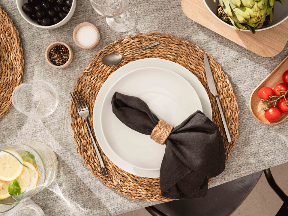 Couverts méditerranéens avec assiette blanche, serviette noire et matières naturelles
