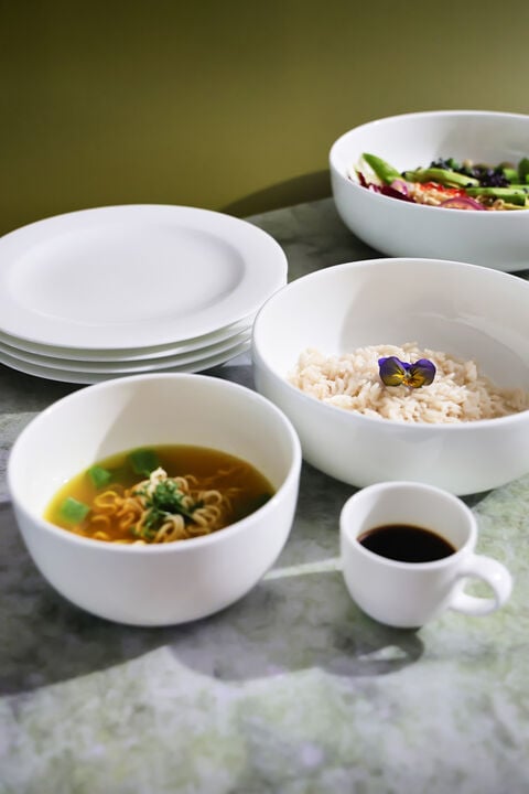 White bowls, plates, and cups next to each other on marble table