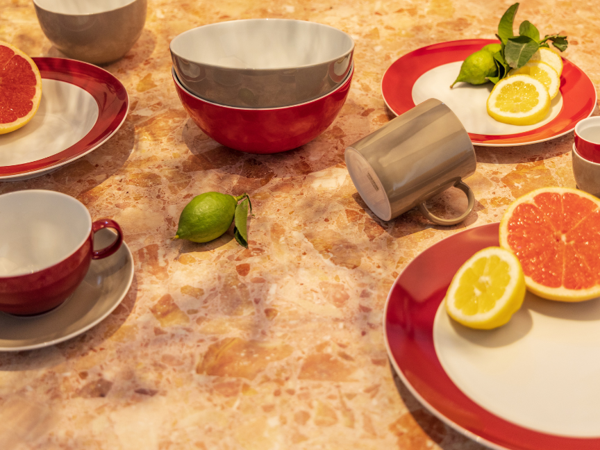 Brunchszene mit Thomas-Geschirr in kr&auml;ftigen Rot- und Cremet&ouml;nen: Auf einer warmen Steinoberfl&auml;che stehen Teller, Tassen und Schalen, arrangiert mit frischen Zitrusfr&uuml;chten wie Grapefruit, Zitrone und Limette. Die Kombination aus farbintensivem Geschirr und frischen Zutaten schafft eine lebendige, moderne Tischatmosph&auml;re.