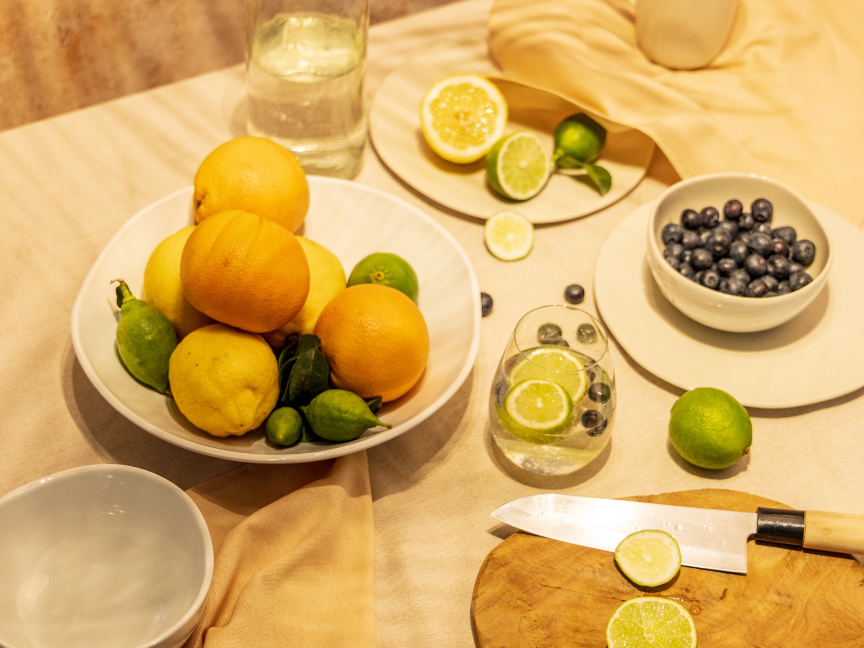 Mediterranes Geschirr von Thomas mit Zitrusfr&uuml;chten, Blaubeeren und einem Glas Wasser mit Limette &ndash; eine sommerliche Tischdekoration in warmen Naturt&ouml;nen.