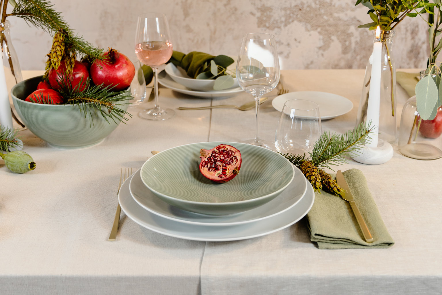 Halber Granatapfel auf dezent grünem Suppenteller, auf zwei weißen Speisetellern auf einem weihnachtlich gedeckten Tisch