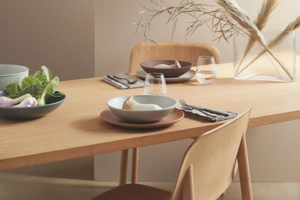 Eine minimalistische Tischdekoration mit einem Holztisch und St&uuml;hlen sowie Geschirr von Thomas Clay