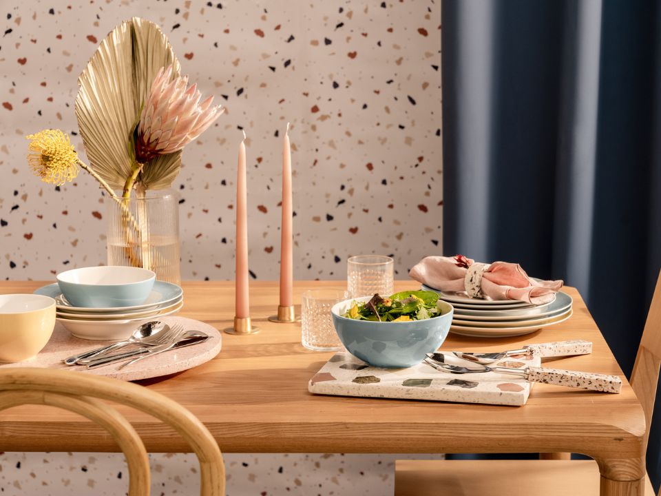 Stilvoll gedeckter Brunch-Tisch mit Thomas-Geschirr auf einer Holzoberfl&auml;che: Pastellfarbene Schalen, Teller und Tassen sind harmonisch arrangiert, erg&auml;nzt durch Brot, Aufstrich und frische Blumen in einer Vase.
