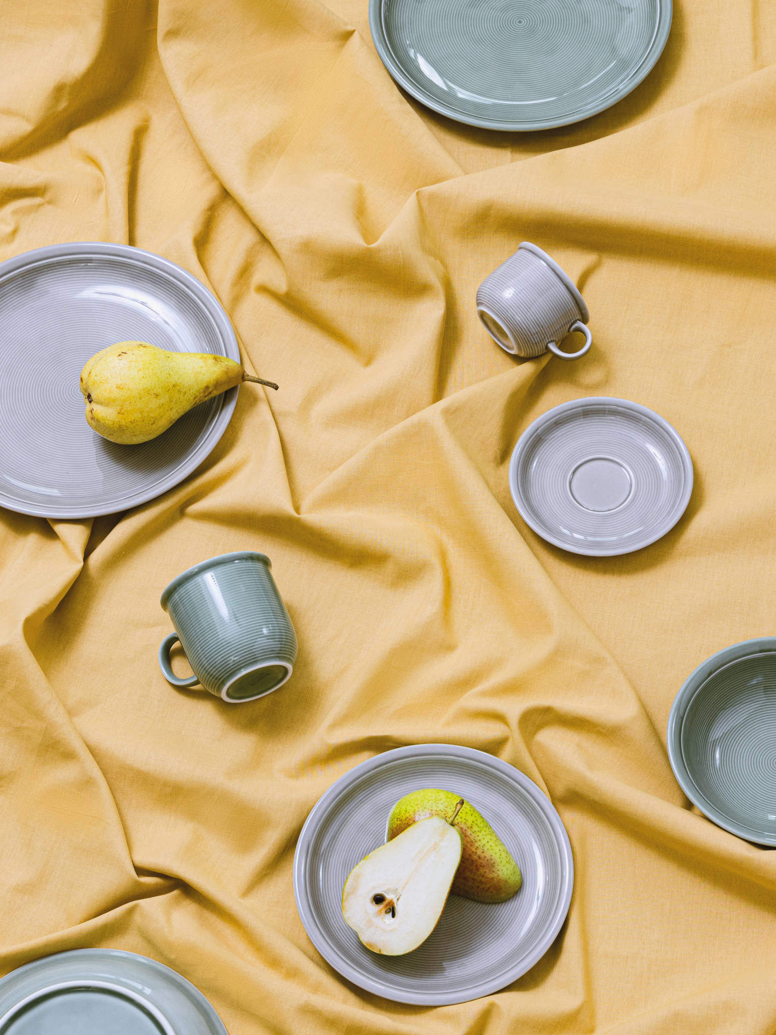Trend Moon Grey Porzellanartikel auf gelber Tischdecke quer beet verteilt und mit Birne dekoriert