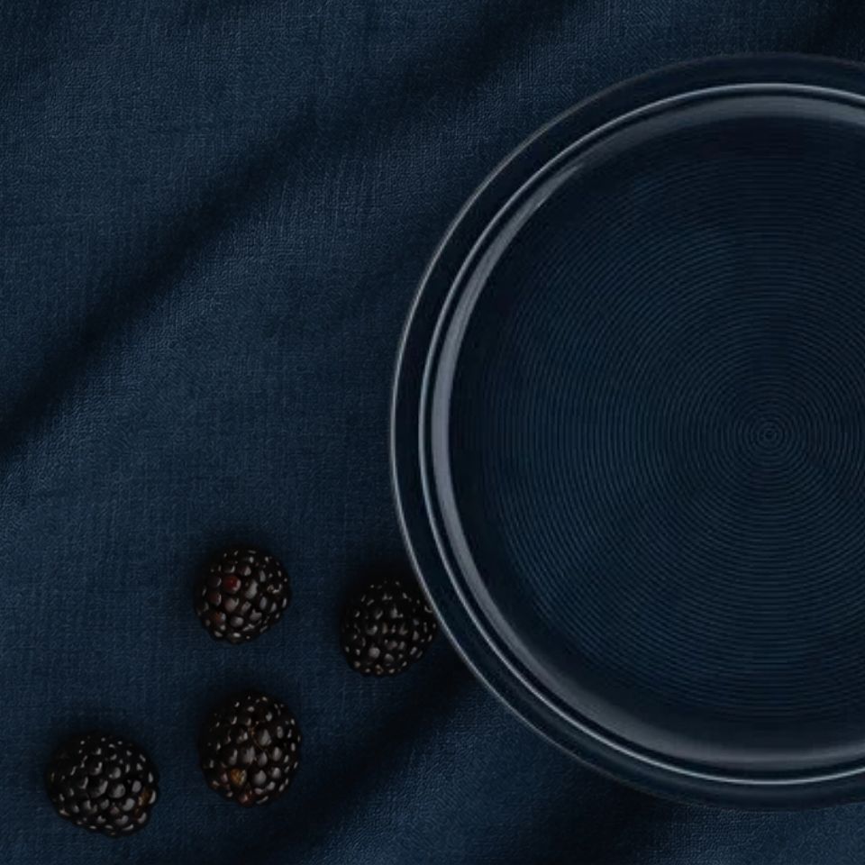 Dunkelblauer Teller mit Brombeeren daneben auf dunkelblauem Hintergrund 