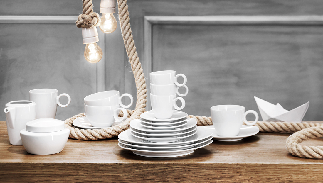 Espressotassen, Kaffeetassen und Untersetzer von Thomas Vario gestapelt auf einem Holztisch mit zwei Glühbirnen als Licht- und Dekoelemente