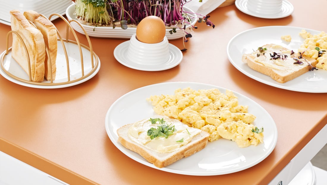 Brotteller mit Toast neben Frühstückstellern mit Ei Rührei und Toast