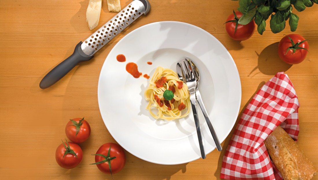 Amici Pastateller mit Nudeln angerichtet auf einem Tisch mit Tomaten, Brot und Parmesan