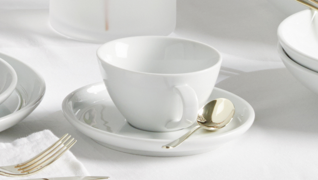 Weiße Tasse auf gedecktem Tisch mit weißer Tischdecke